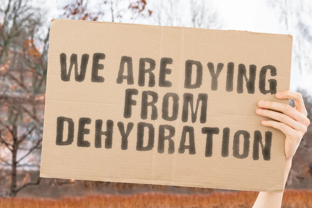 The phrase " We are dying from dehydration " on a banner in men's hand with blurred background. Destruction. Die. Dramatic. Ecosystem. Exhaustion. Healthcare